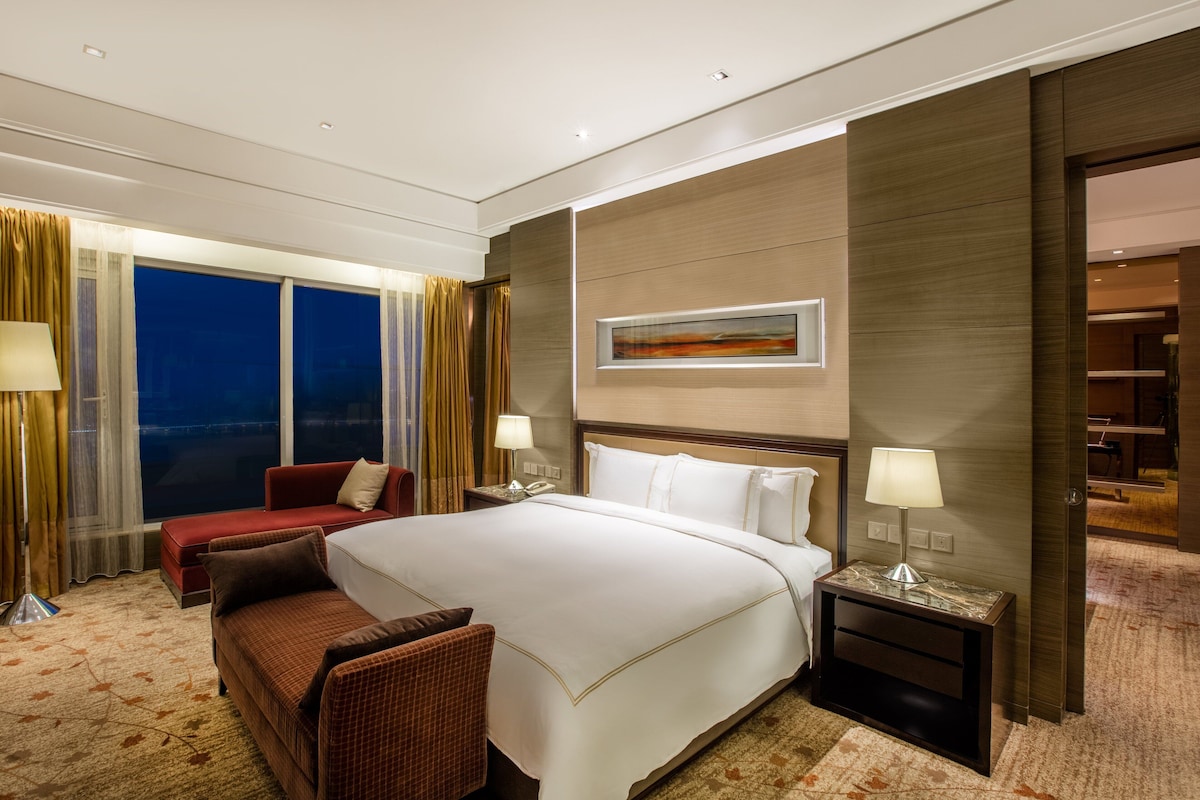 Ein Hotelzimmer mit einem großen Bett, einem roten Sofa, einem kleinen Tisch und einem Nachttisch.