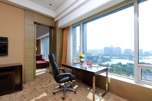 Ein moderner Büroraum mit großem Schreibtisch, zwei Stühlen, einem Fernseher und Blick auf eine Skyline und einen Fluss.