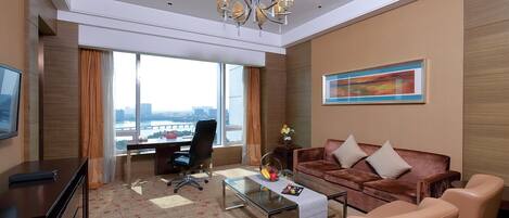A modern hotel room with a large window, a desk, a sofa, and a coffee table.