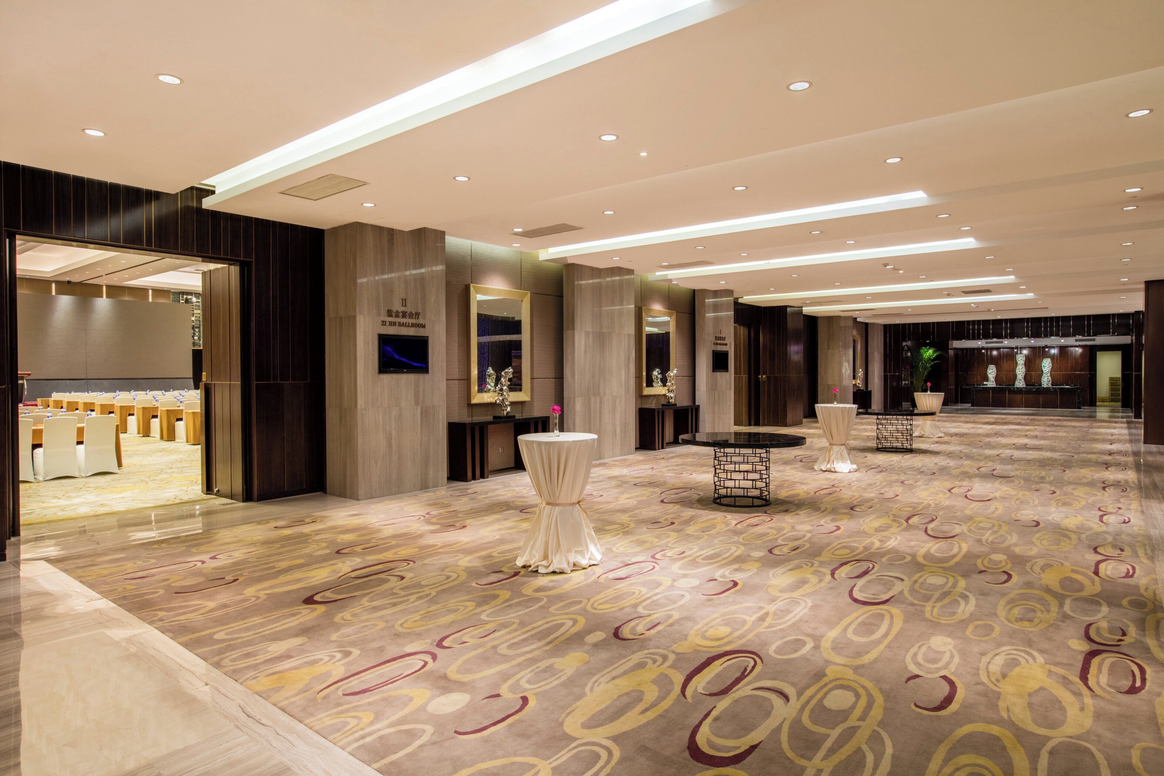 Un vestíbulo de hotel con alfombra estampada, un mostrador de recepción y una zona de estar con mesas y sillas.