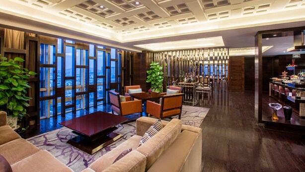 Een moderne hotellobby met een zithoek, een bar en uitzicht op de stad door grote ramen.