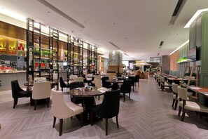 Un restaurant spacieux, doté de nombreuses tables et chaises, d’un espace cuisine avec un comptoir et d’un téléviseur fixé au mur.
