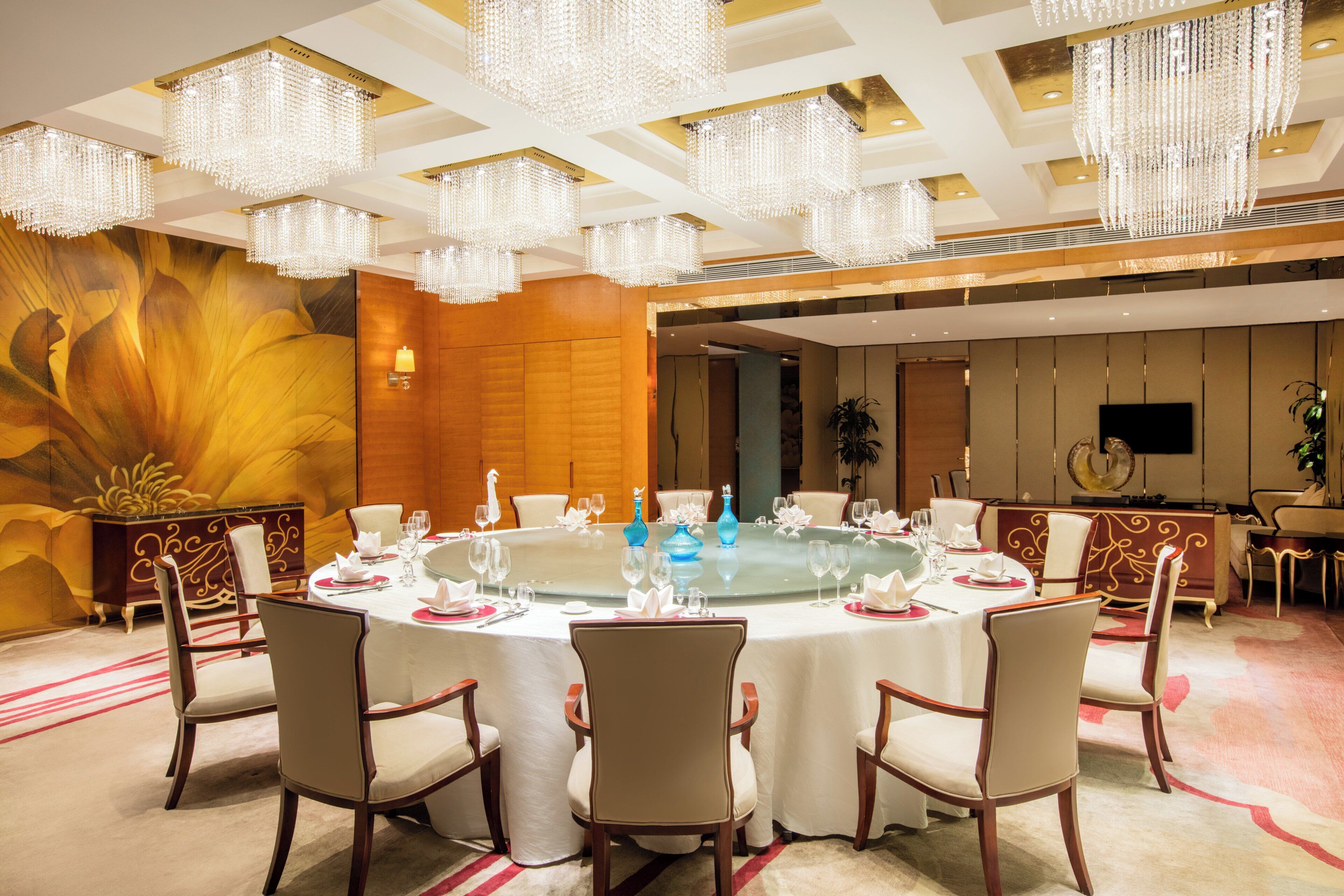 A formal dining room with a round table, chairs, and a large floral mural on the wall.