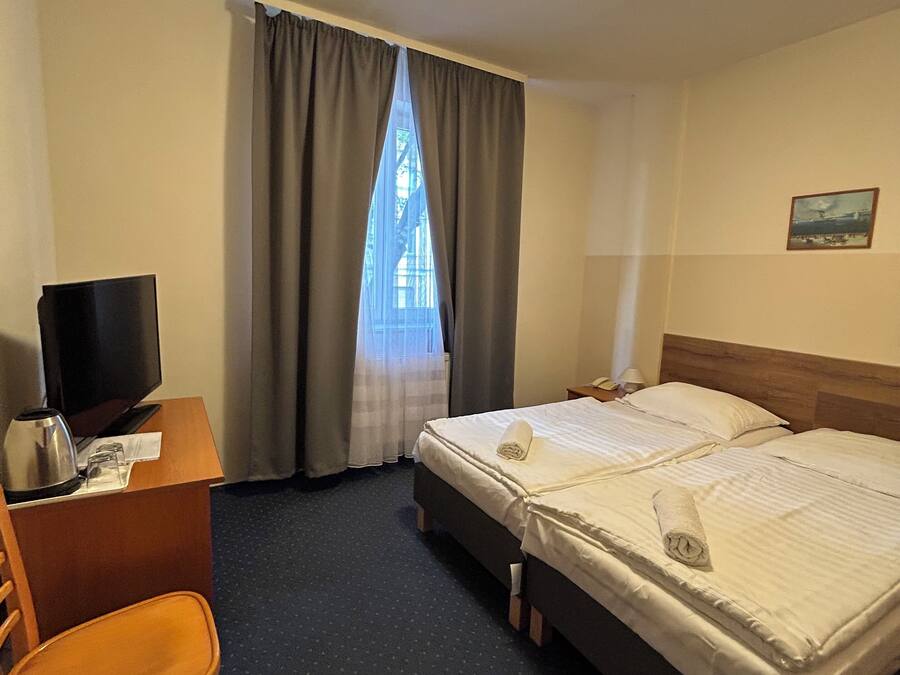 A hotel room with a single bed, a desk with a television, and a chair.