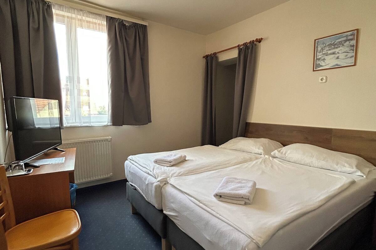 Una habitación de hotel con cama, escritorio, silla, televisor y ventana con cortinas.