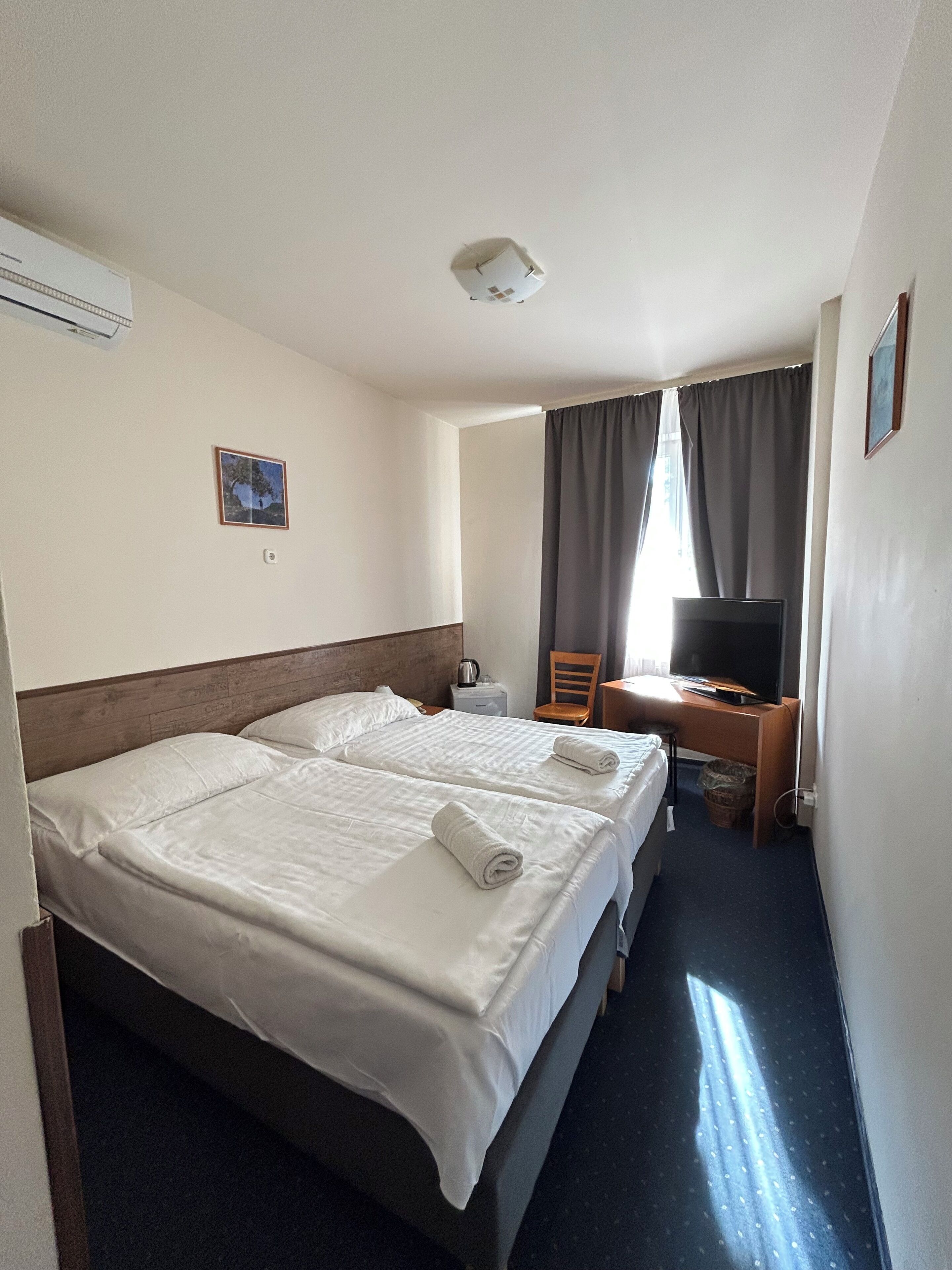 Habitación de hotel con dos camas, un escritorio con silla, televisión y ventana con cortinas.