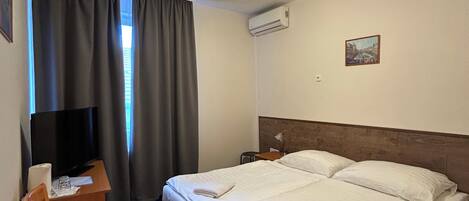 A hotel room with a bed, a desk with a chair, a TV, and a window with curtains.