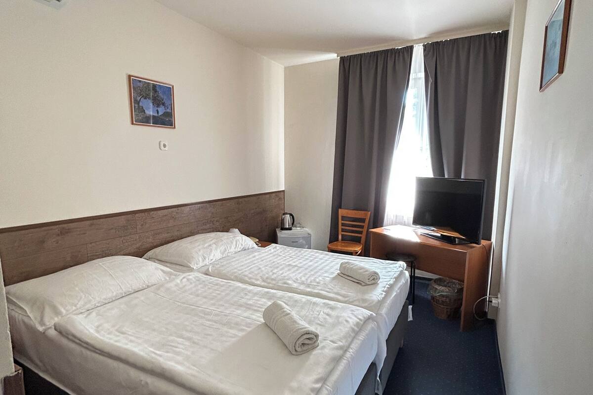 Habitación de hotel con dos camas, un escritorio, un televisor y una ventana con cortinas.