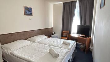A hotel room with two beds, a desk, a TV, and a window with curtains.