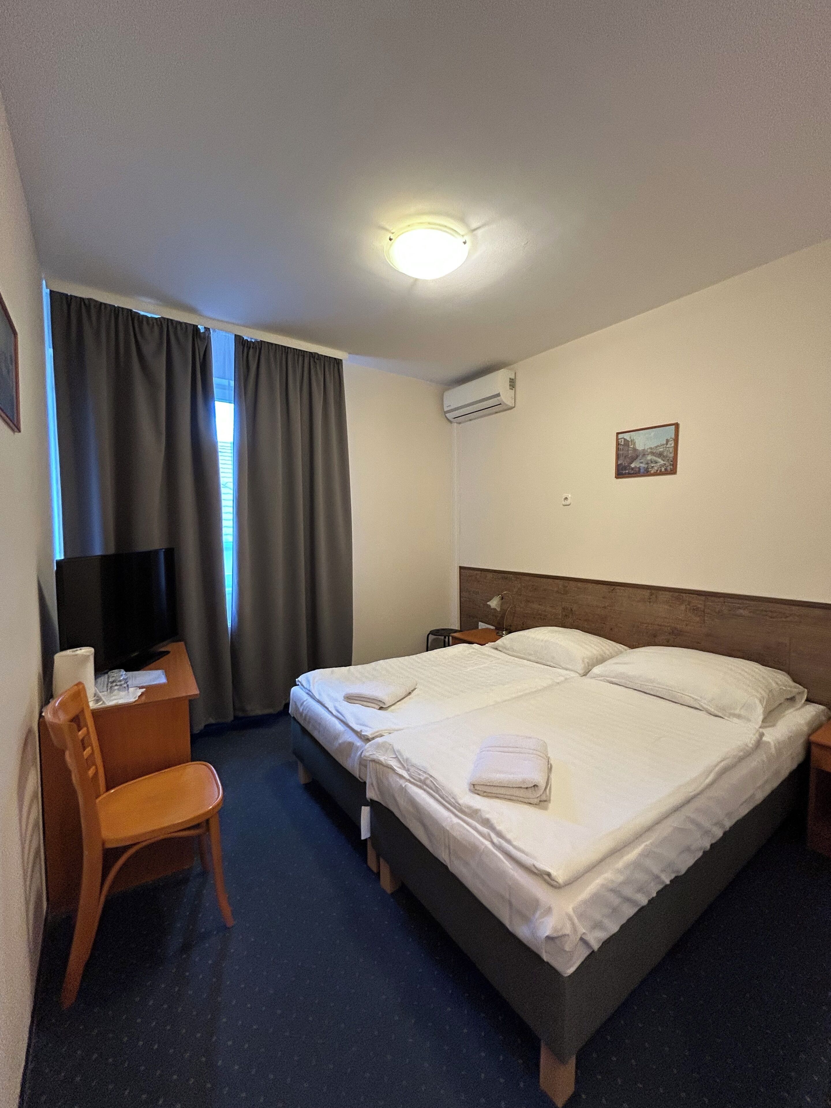 Una camera d'albergo con un letto, una scrivania con una sedia, una televisione e un condizionatore d'aria.