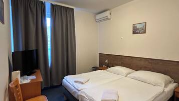 Una camera d'albergo con un letto, una scrivania con una sedia, una televisione e un condizionatore d'aria.