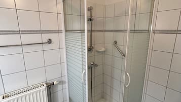 A corner shower with glass doors, a white radiator, and blue-tiled floor.