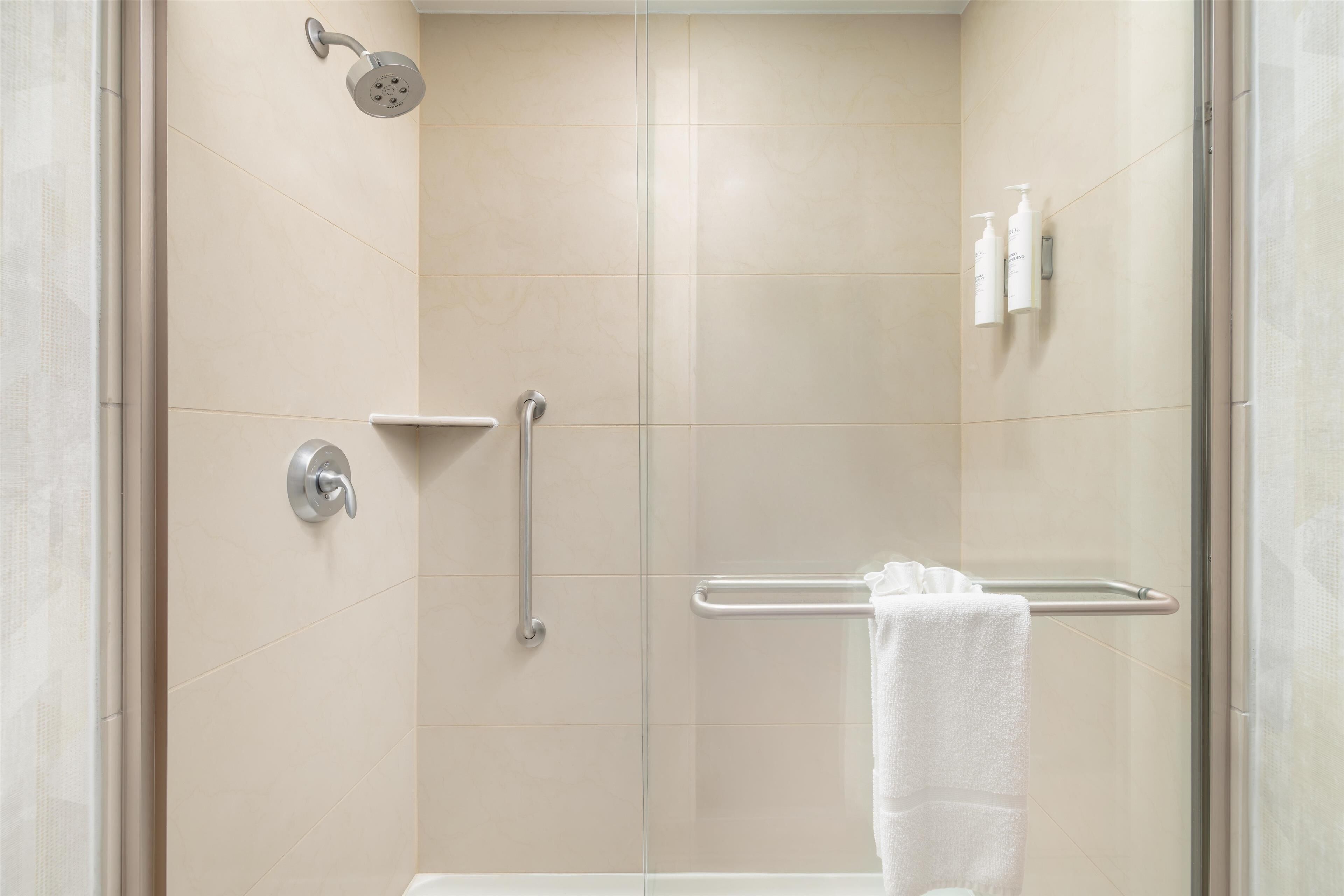 A modern bathroom with a glass shower enclosure, a grab bar, and a towel rack.