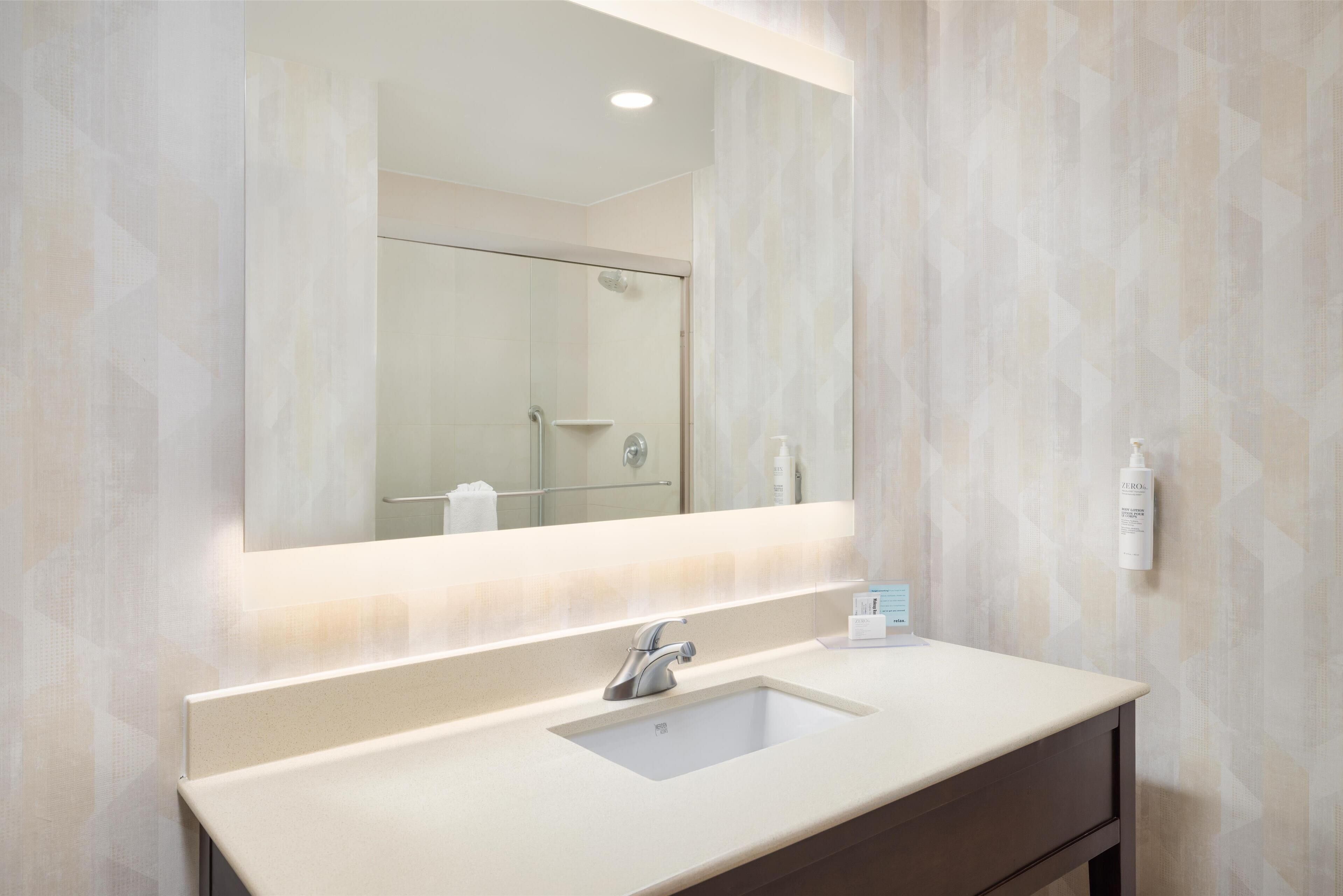 A bathroom with a large mirror, a sink, and a shower.