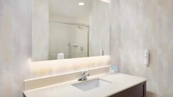 A bathroom with a large mirror, a sink, and a shower.