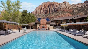 A swimming pool with lounge chairs and umbrellas, a stone fireplace, and a mountain backdrop. - Hampton Inn & Suites Springdale/Zion National Park (Springdale)