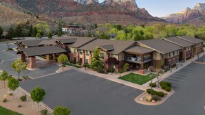 A hotel with a parking lot, surrounded by greenery and mountains in the background. - Hampton Inn & Suites Springdale/Zion National Park (Springdale)