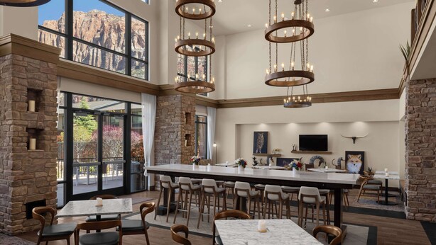 A spacious dining area with high ceilings, stone walls, and large windows offering views of a mountainous landscape. - Hampton Inn & Suites Springdale/Zion National Park (Springdale)