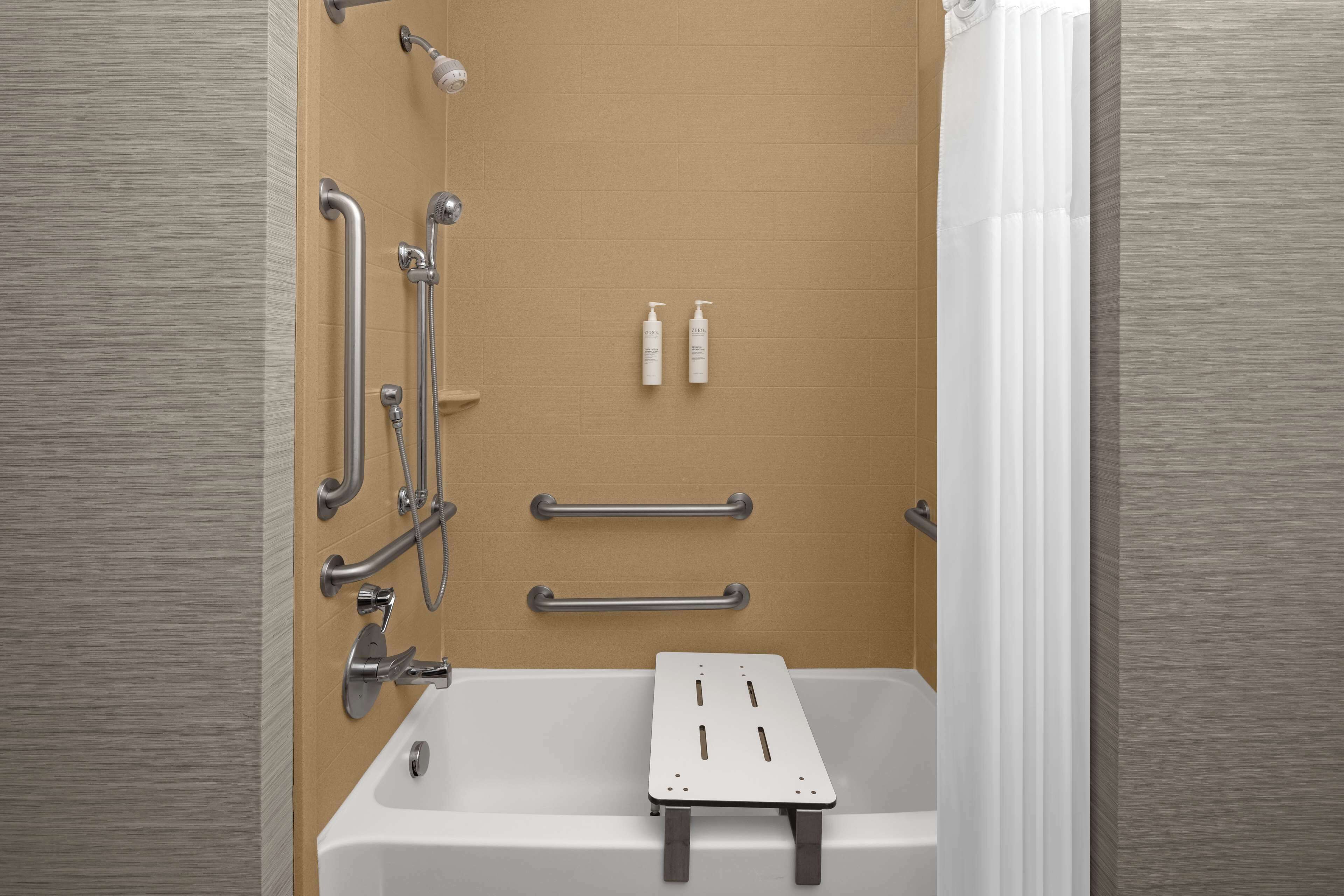 Une salle de bain moderne équipée d’une baignoire, de barres d’appui et d’un pommeau de douche.
