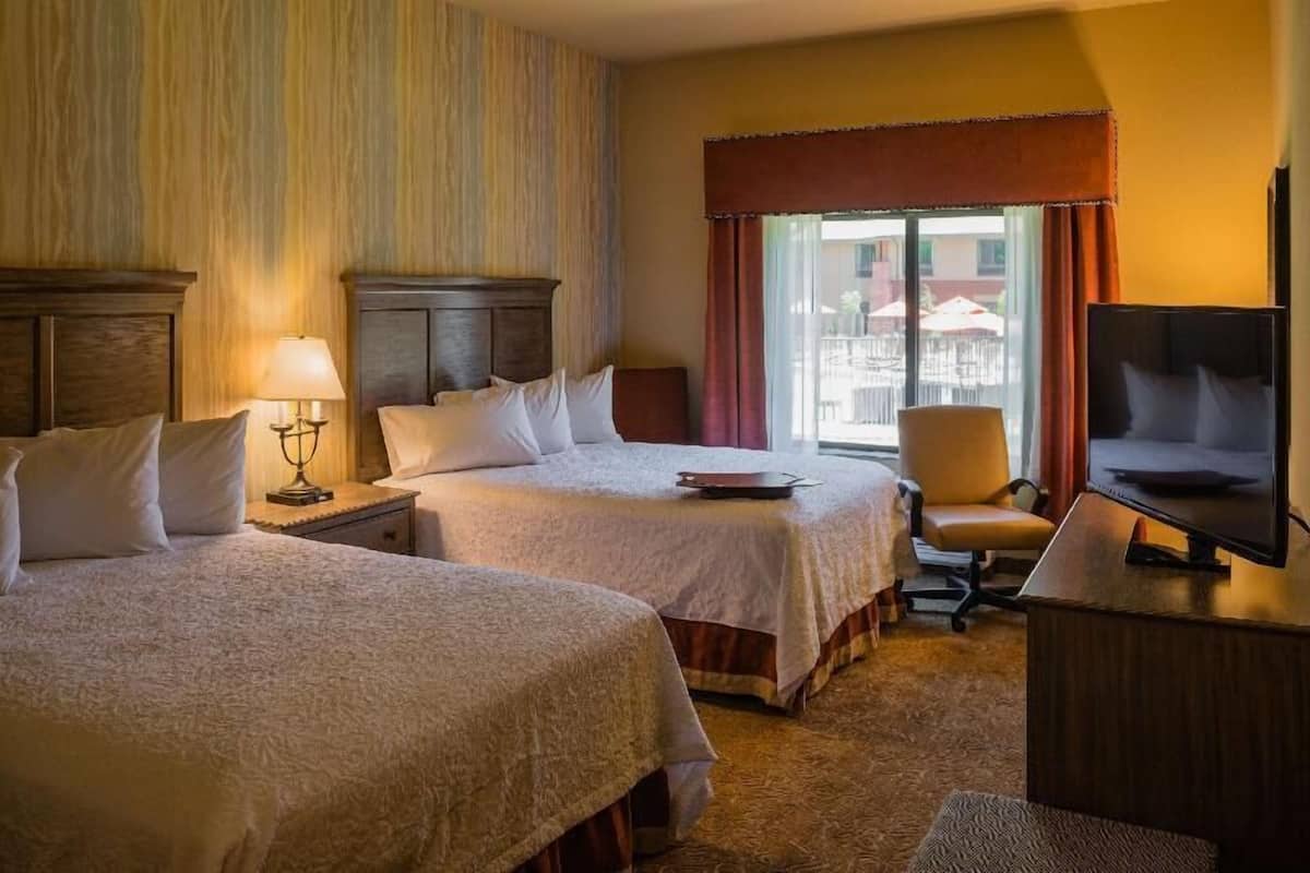 Habitación de hotel con dos camas, un escritorio con televisor, una silla y una ventana con cortinas.