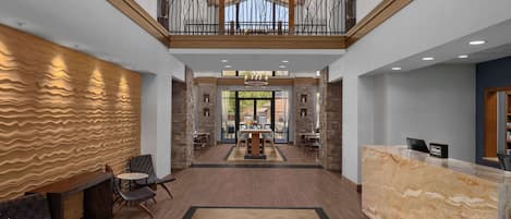 A spacious lobby with a herringbone-patterned wall, a reception desk, and a balcony with a railing.