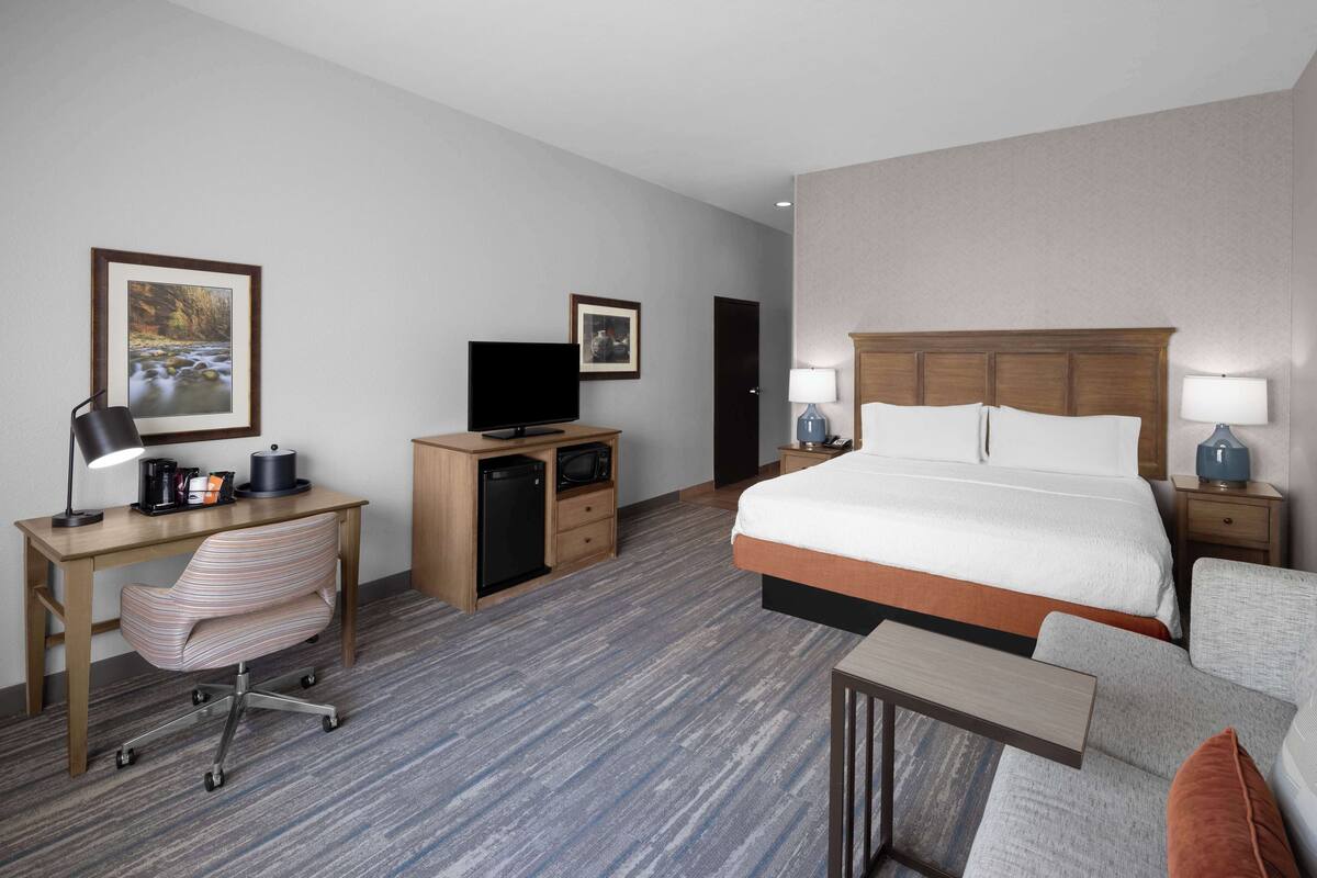Habitación de hotel con una cama grande, un escritorio con computadora, una silla, un televisor y una mesita.
