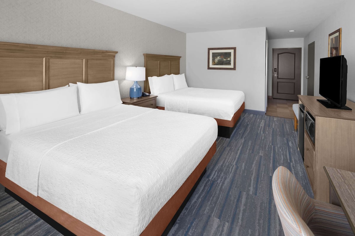 Habitación de hotel con dos camas, un escritorio, un televisor y la puerta del baño.