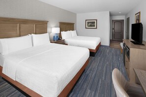A hotel room with two beds, a desk, a television, and a bathroom door.
