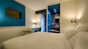 Una camera d'albergo con un letto grande, una scrivania, una sedia, una TV a muro e un bagno con lavandino e specchio.