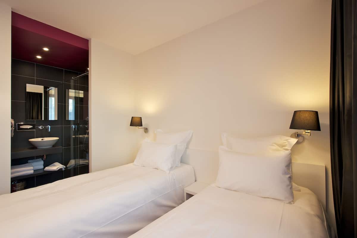 A hotel room with two beds, a bathroom with a glass shower enclosure, and a vanity with a sink.