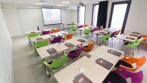 Una sala conferenze con diversi tavoli e sedie colorate, dotata di computer portatili e bottiglie d'acqua.