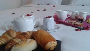 A neatly arranged breakfast setup on a bed with croissants, a teapot, cups, and a tray with pastries and jams.