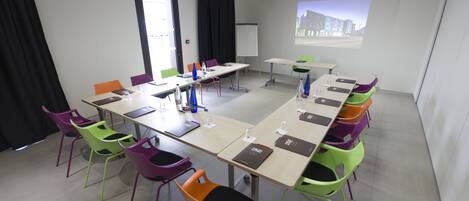 A conference room with a long table, colorful chairs, a projector screen, and a whiteboard.