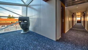 Un corridoio d'hotel moderno con una parete in vetro e una scultura a pavimento.