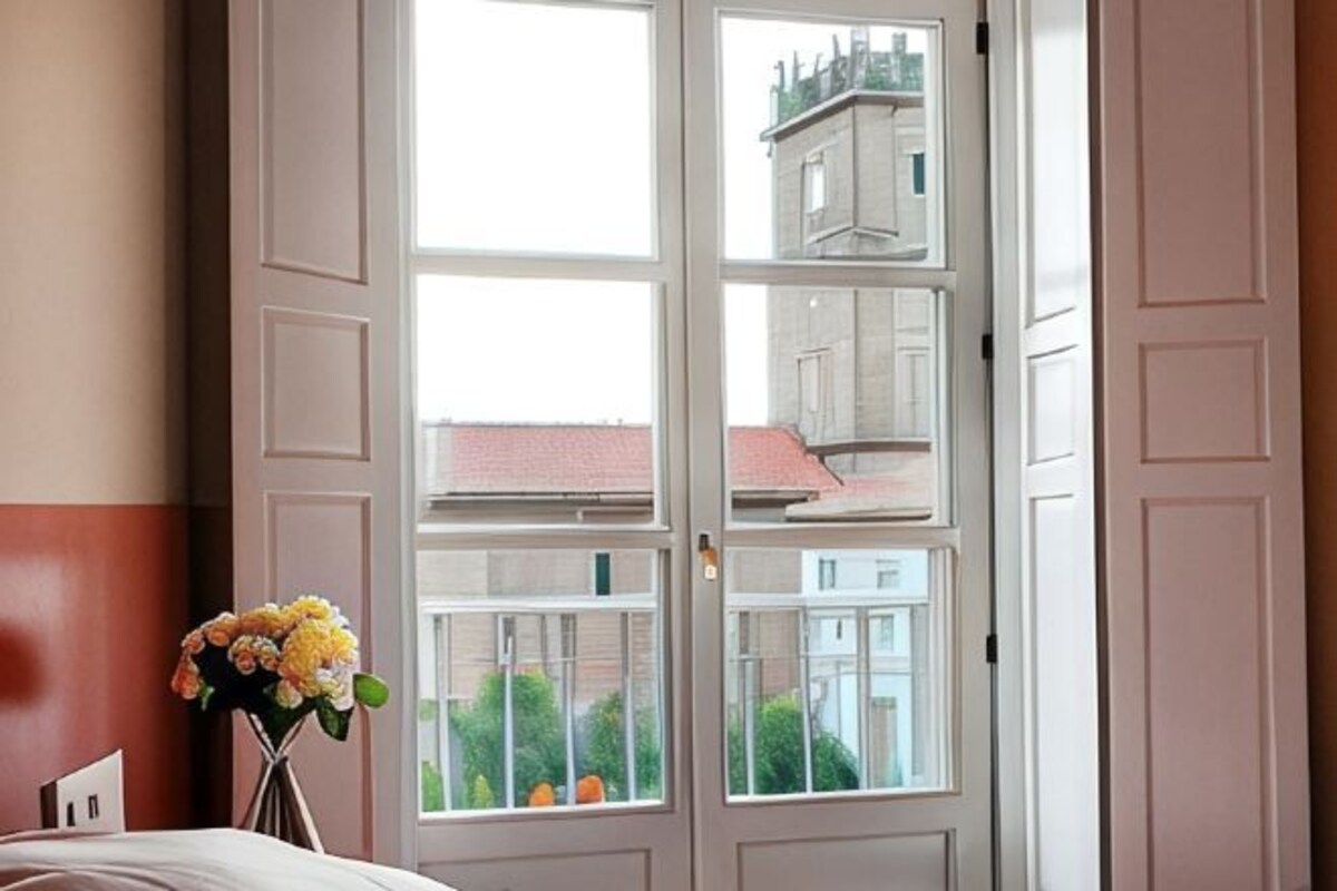 A room with a large window, a bed, and a vase with flowers.