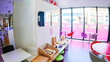 Un espacio interior luminoso con un amplio ventanal, mesas, sillas y un tablero de ajedrez.