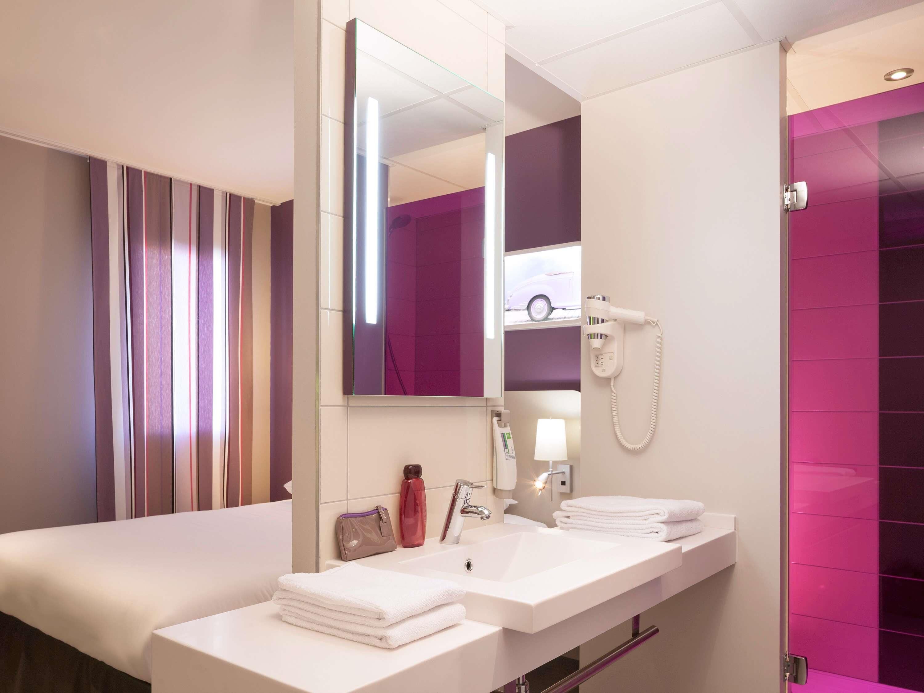 A hotel bathroom with a double sink, a mirror, a hairdryer, and a towel rack.