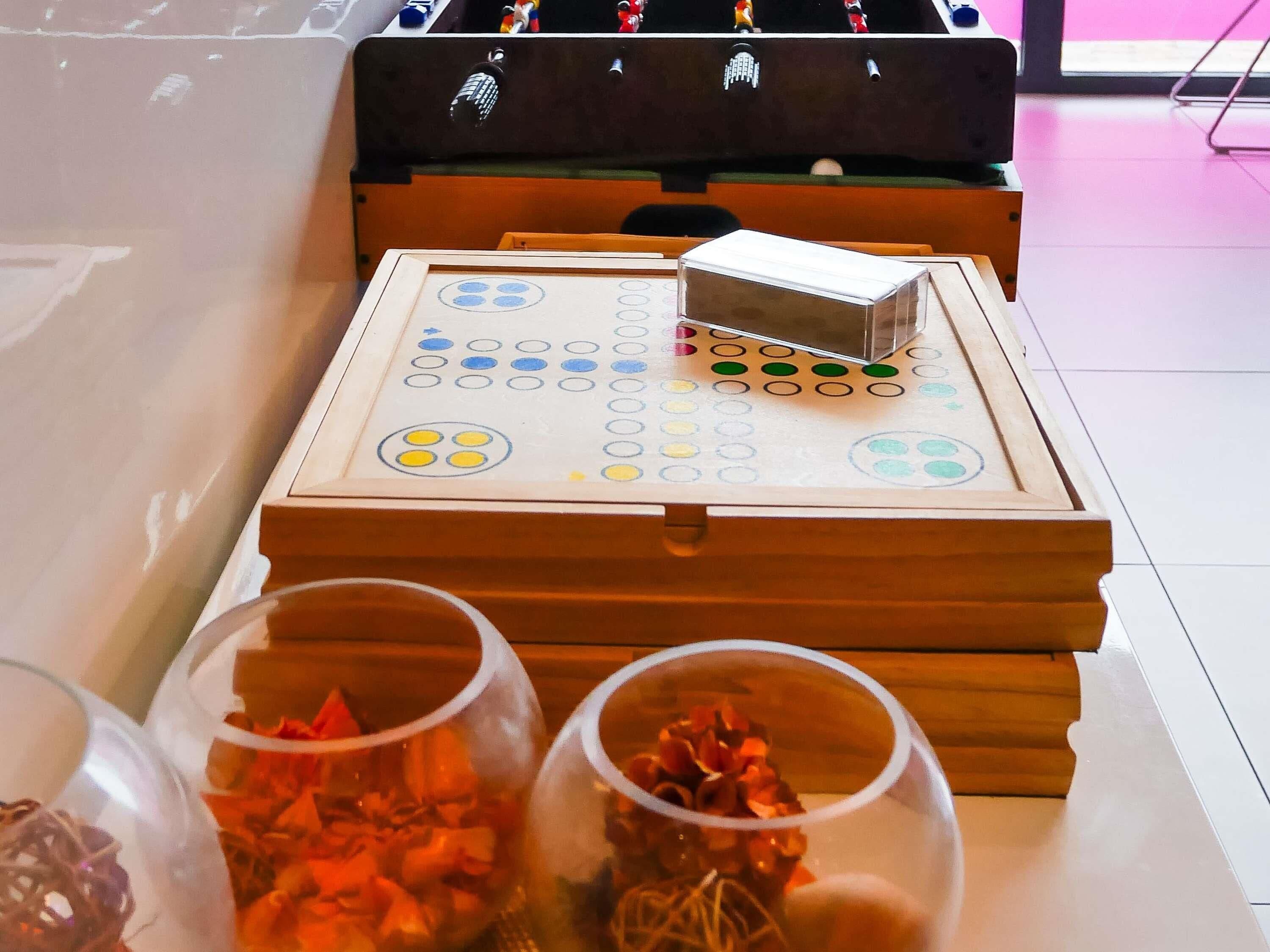 A wooden board game table with a game board and pieces, surrounded by glass containers with items.