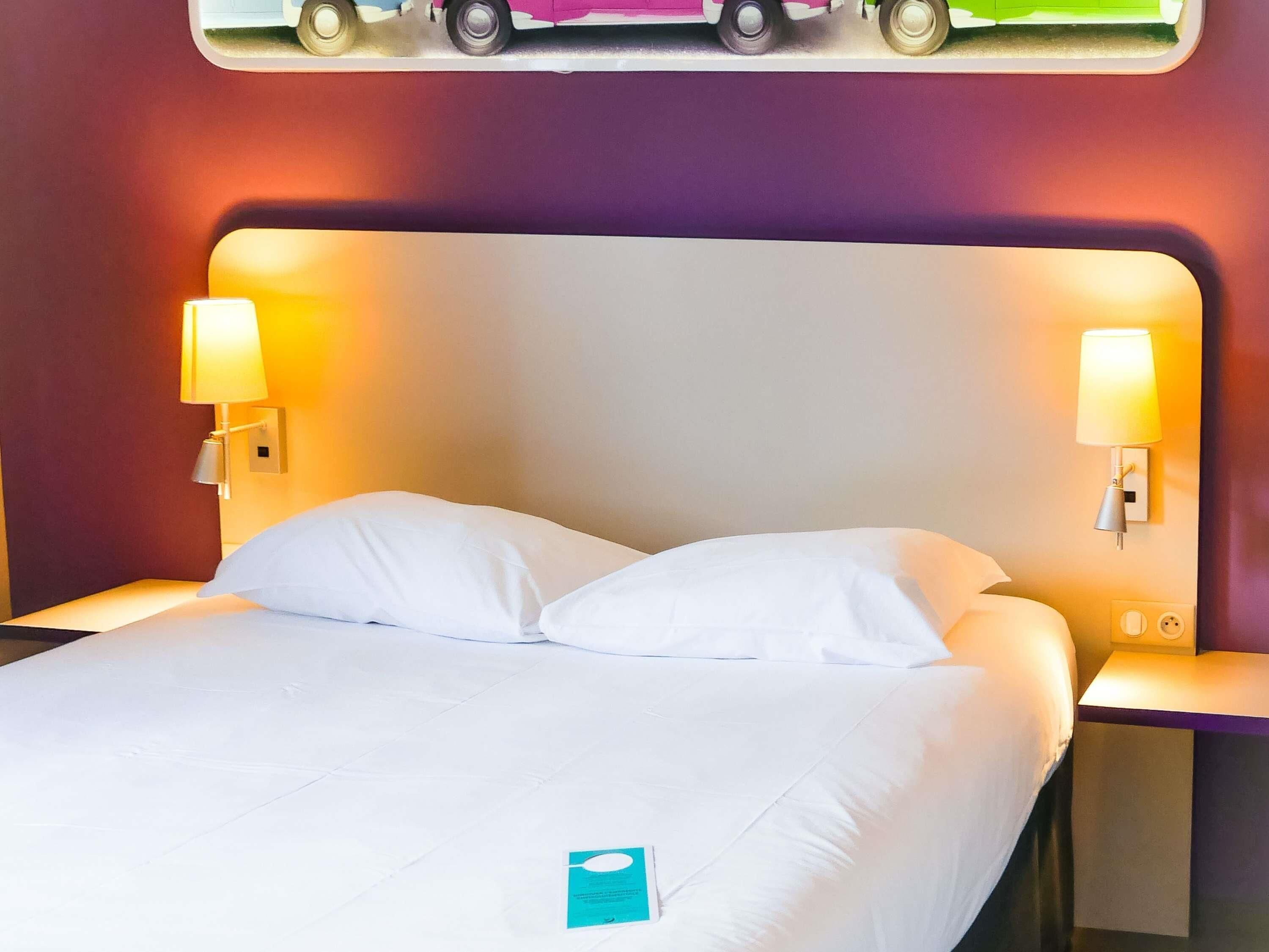Une chambre d’hôtel avec un lit, deux lampes de chevet et une œuvre d’art accrochée au mur.