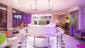 Un bar moderno con una mesa redonda central rodeada de taburetes, diversas botellas de licor en estanterías y una planta grande en maceta.
