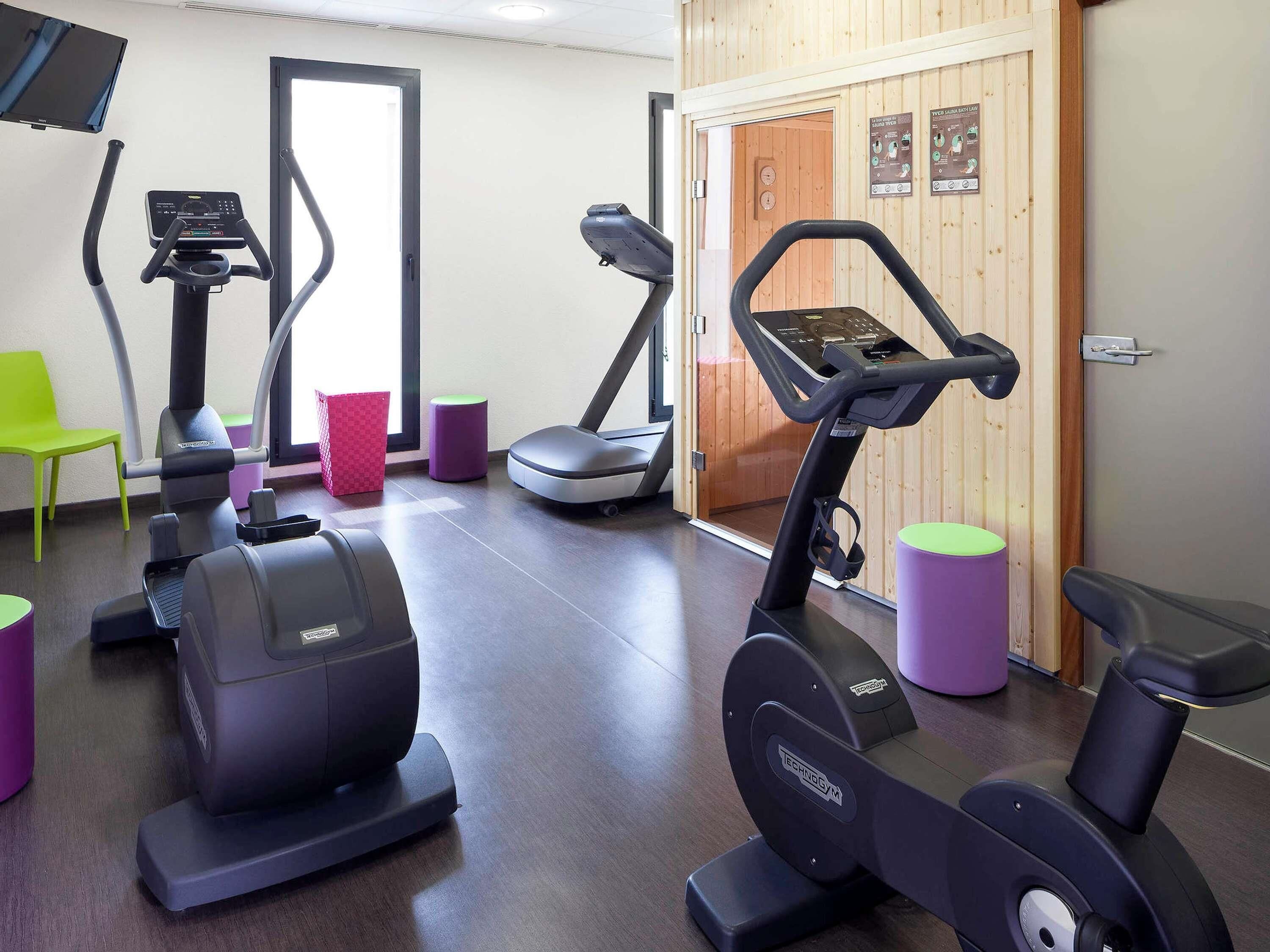 A gym with stationary bikes, treadmills, and a television screen.