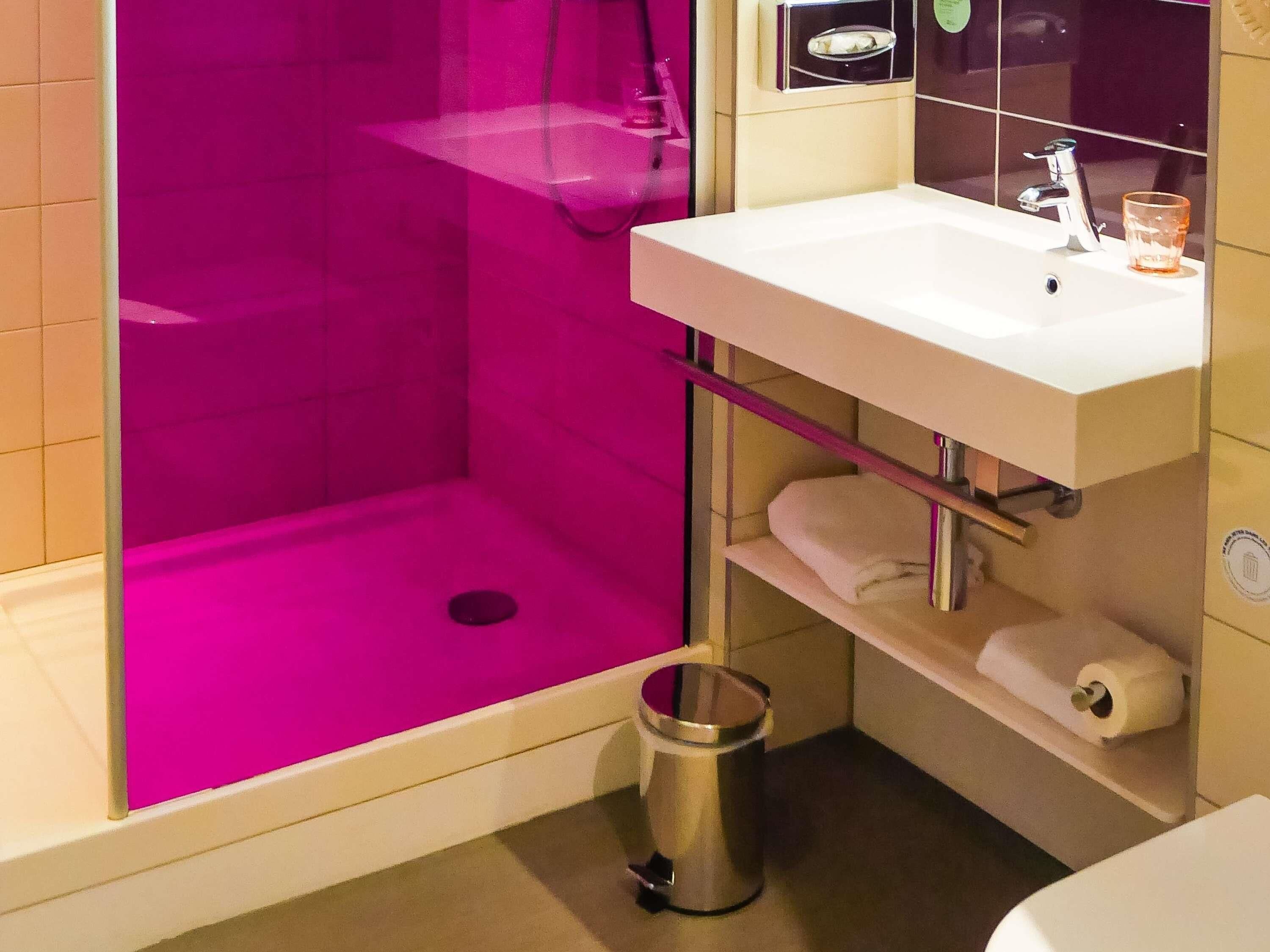 Ein Badezimmer mit einer rosa Duschkabine, einem weißen Waschbecken und einem Mülleimer.