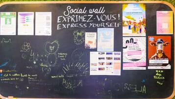 A social wall with various posters and writings, including event announcements and personal messages.