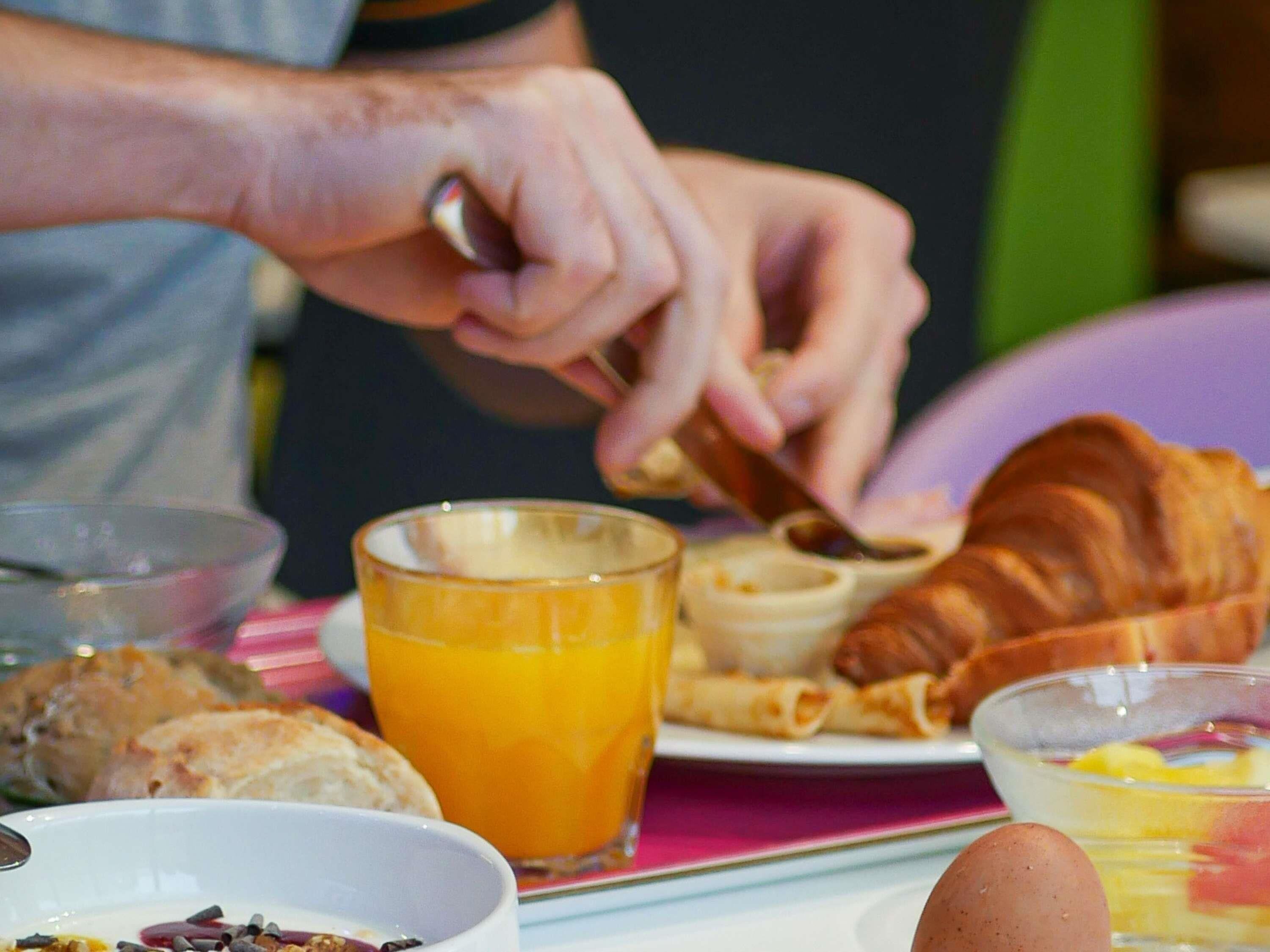 Mesa de café da manhã com prato de comida, copo de suco de laranja e um croissant.