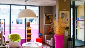 Un interior moderno con una mesa redonda blanca, una silla verde, un florero rosa alto y una lámpara colgante blanca de gran tamaño.