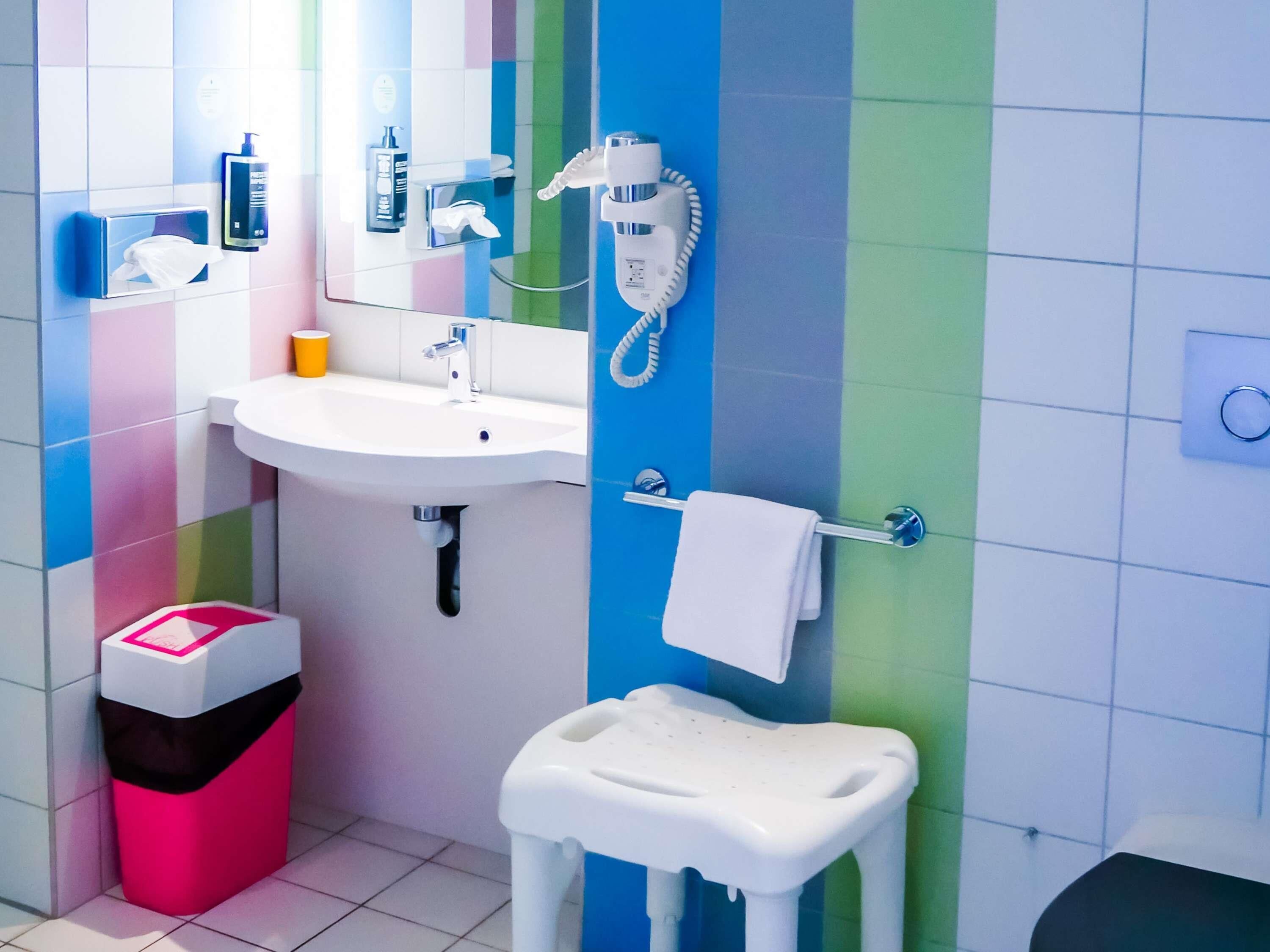 Un baño con lavamanos blanco, un espejo, un teléfono y un cesto de basura.