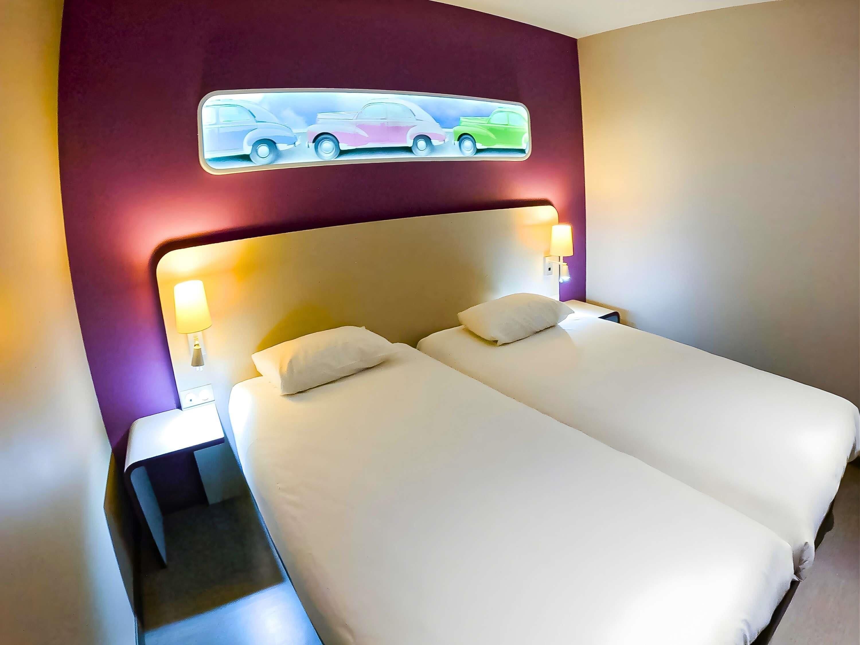 A double bed with white linens, two bedside lamps, and a wall-mounted artwork of cars.