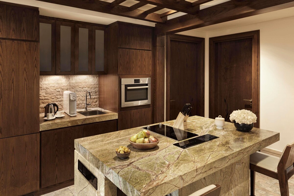 Une cuisine moderne avec des meubles de couleur sombre en bois, un plan de travail en marbre, un four encastré et un évier.