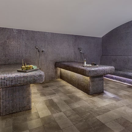 A modern bathroom with a tiled floor, a bench, a sink, and a shower area.
