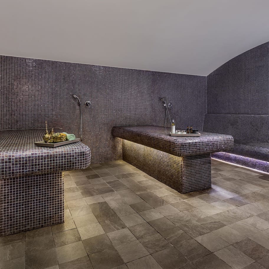 A modern bathroom with a tiled floor, a bench, a sink, and a shower area.